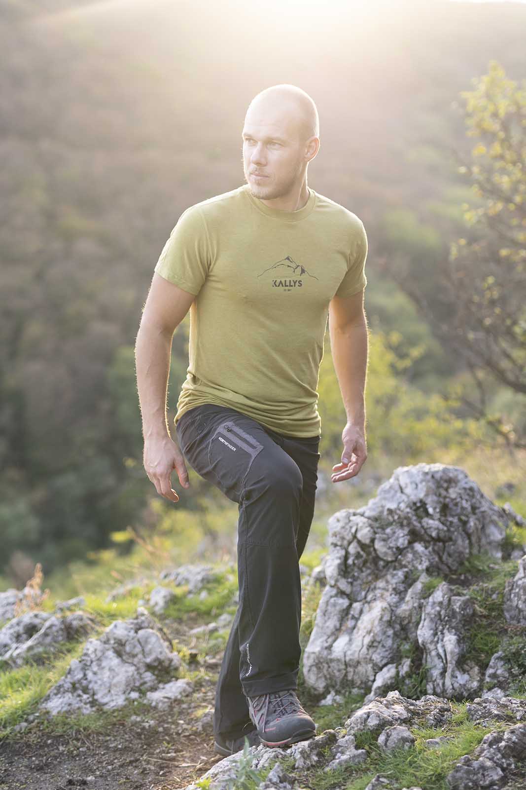 Muž počas západu slnka vystupuje na kopec. Má oblečené zelené tričko značky kallys, ktoré sa nazýva Supreme Silk a je z merina a tencelu