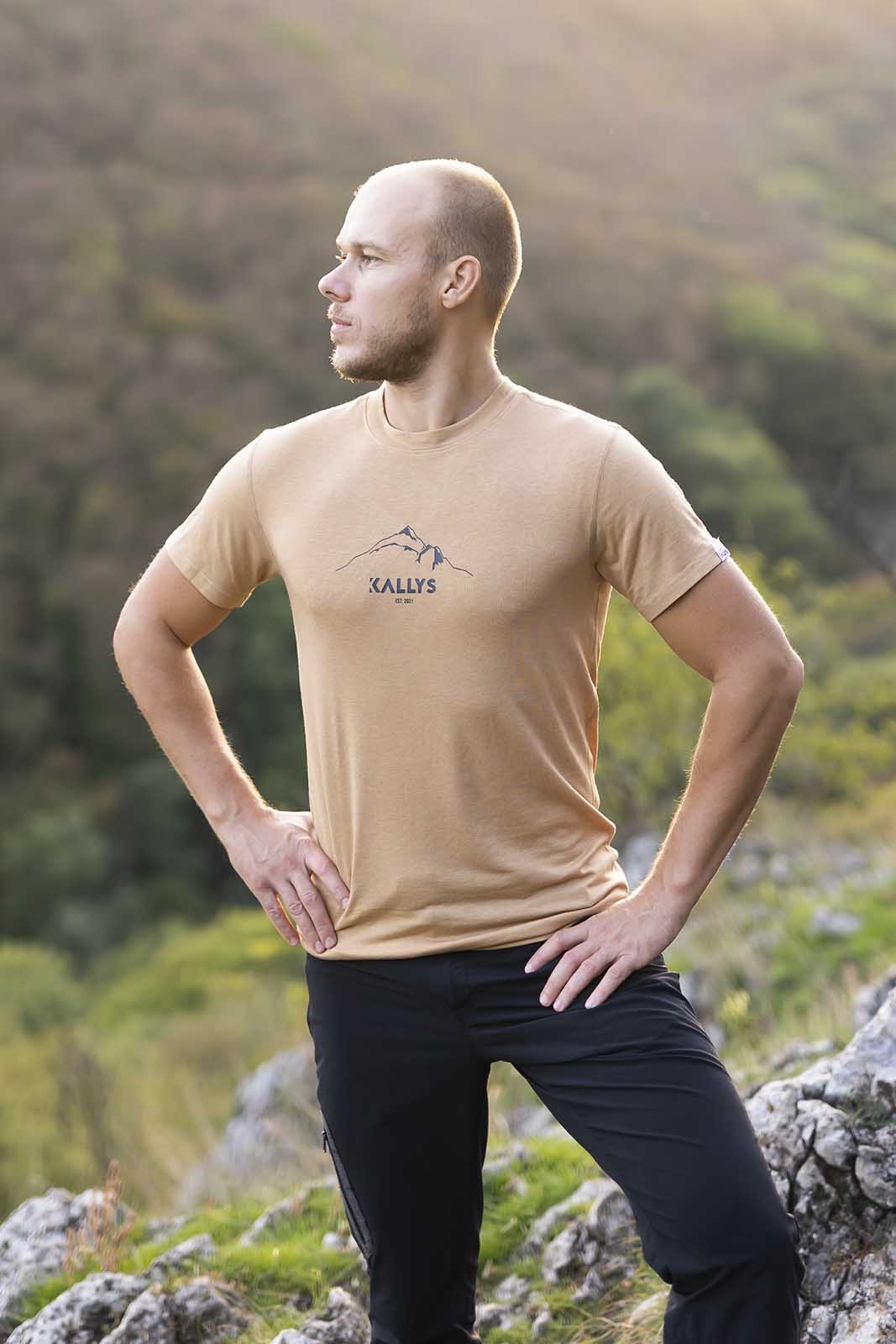 Muž stojaci na kopci s rukami vbok hľadí na západ slnka. Na sebe má hnedé merino tričko s krátkym rukávom značky kallys.