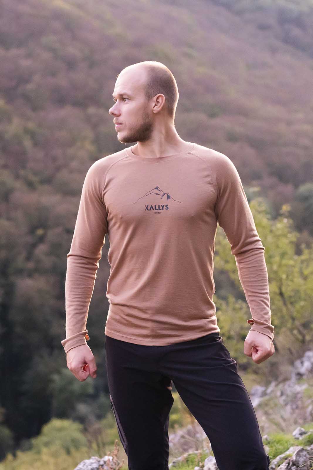Muž stojí na kopci hľadí do boku. Má na sebe hnedé merino tričko s dlhým rukávom od značky kallys