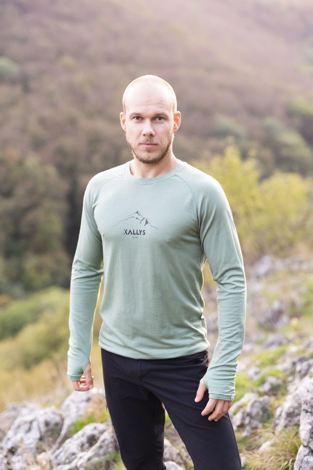 Muž stojí na kopci a má na sebe tričko s dlhým rukávom značky kallys. Tričko je mentolovo zelenej farby zo 100% merina